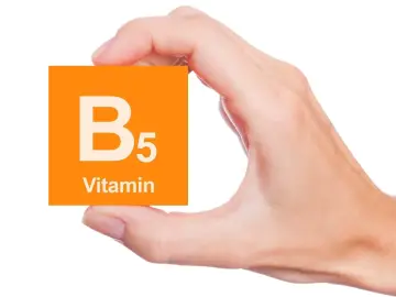 Dłoń trzyma pomarańczową kartkę z napisem "B5 Vitamin". To ważny składnik, jak kwas pantotenowy.